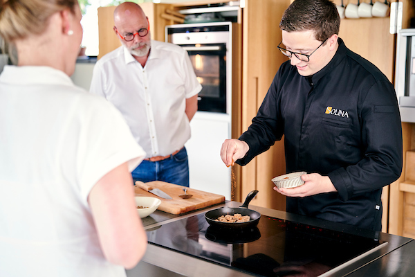 Un chef cuisinier cuisine devant deux individus.